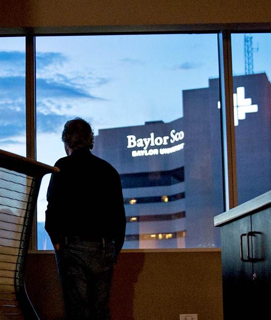 A man stands in silhouette in front of a window overlooking Baylor Scott & White Heart and Vascular Hospital in Dallas.